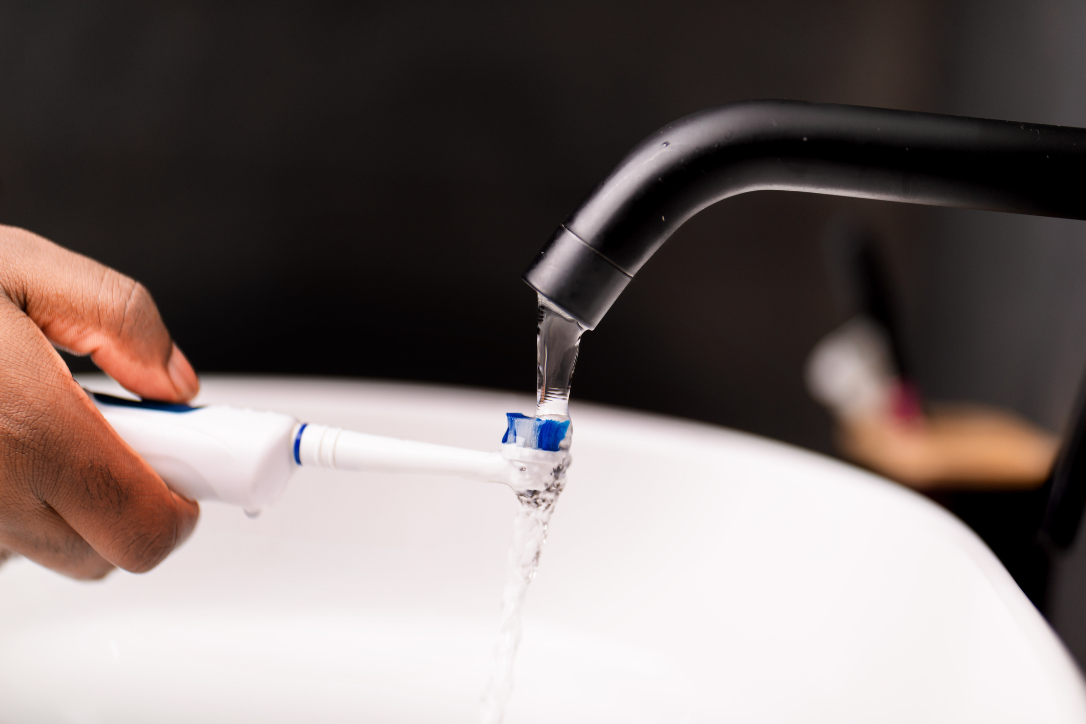hand-rinsing-electric-toothbrush-under-bathroom-faucet-for-dental-hygiene